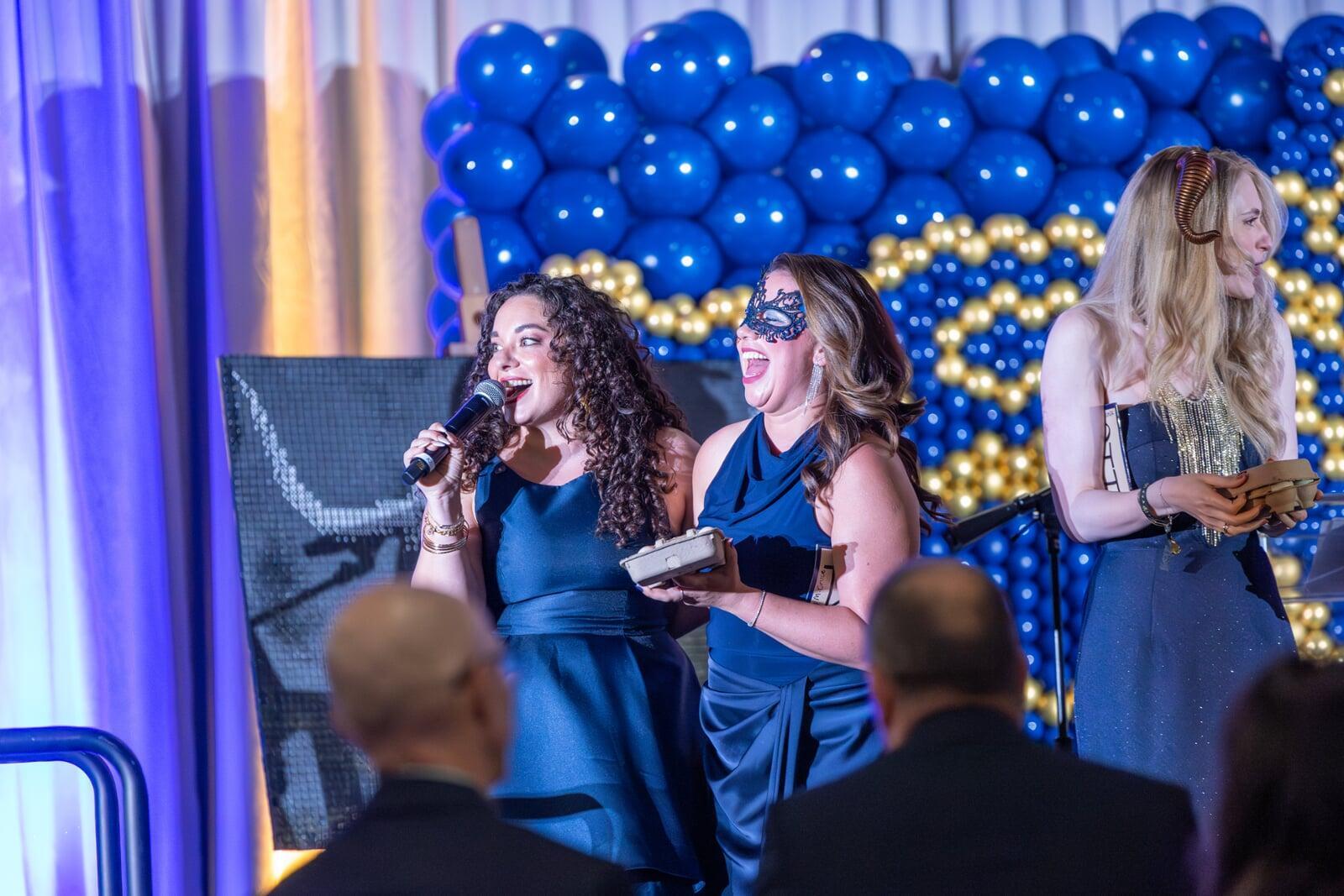 Micki P in a navy evening gown holding Microphone